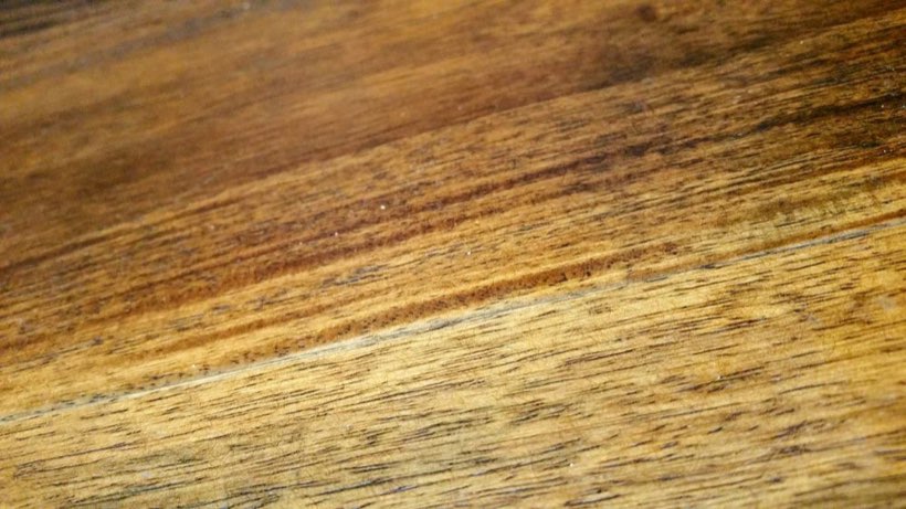Dark staining and a swollen board edge where water has sat on an oak floor.
